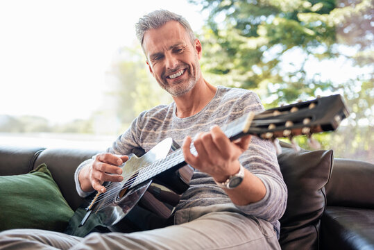 Man playing guitar and smiling at home during leisure time