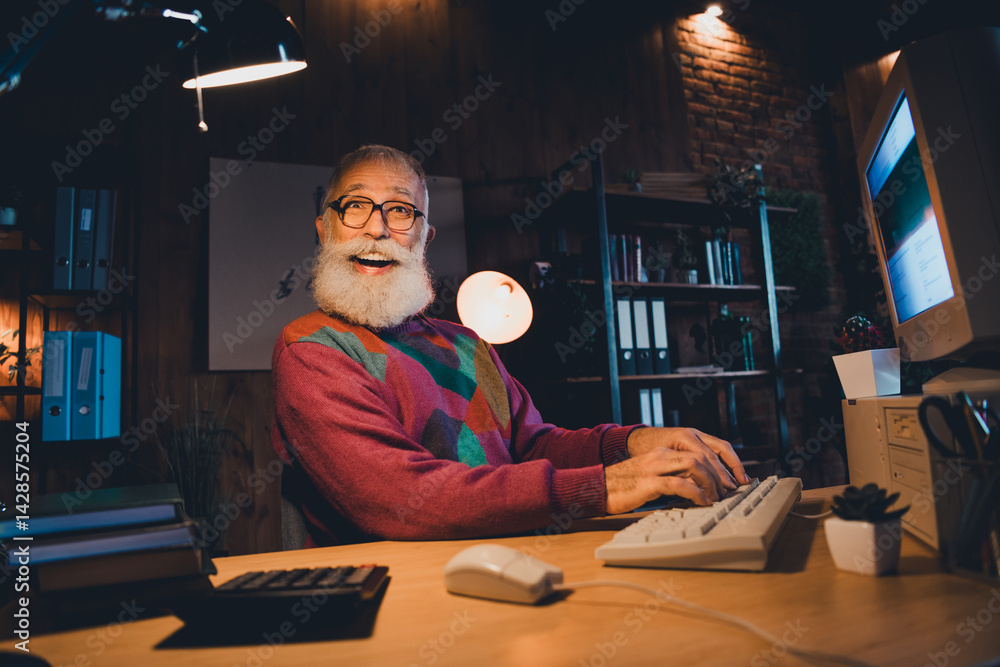 Poster elderly male programmer working at home office in the evening using a computer, providing a sense of