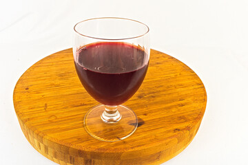 A refreshing glass of grape juice sits on a wooden cutting board against a clean white background. The image is a simple, yet elegant presentation.