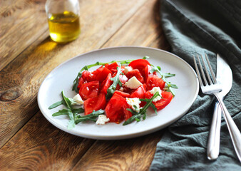 Salad with tomatoes, cheese and arugula in a plate on the table