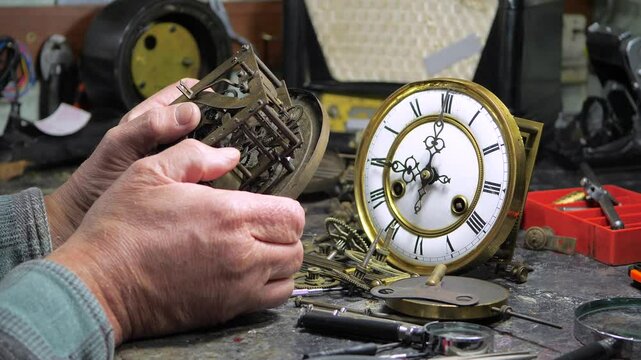 An elderly craftsman, in a workshop, repairs an old clock mechanism, an antique watch, adjusts gears, lubricates them with oil, cleans them from dust and dirt. Slow motion.
