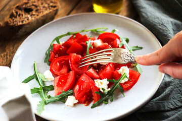 Salad with tomatoes, cheese and arugula in a plate on the table