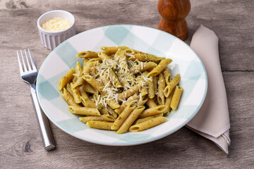 Italian pasta penne on a plate with pesto sauce and parmesan cheese