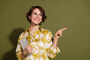 Confident young businesswoman with notebook in hand pointing with a smile against a khaki background