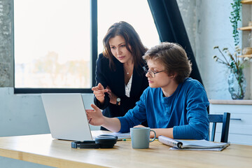 Teenage boy student with female mentor trainer teacher looking at laptop computer screen