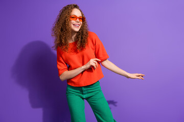 Charming young woman with curly hair wearing trendy outfit posing stylishly against a vibrant purple background