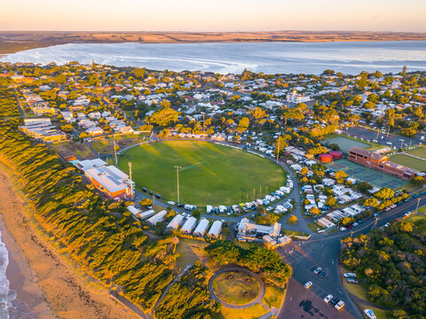 Aerial view of a coastal football oval surrounded by caravans and camp sites