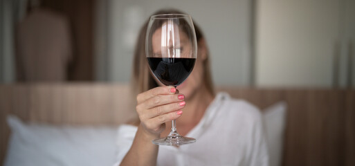 Young beautiful woman with a glass of wine sitting on the bed.