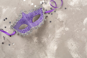 Bright carnival mask with confetti on concrete background, top view