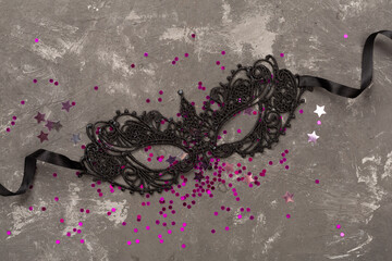 Bright carnival mask with confetti on concrete background, top view