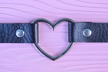 one black leather choker collar with gray metal heart lies on pink table in room