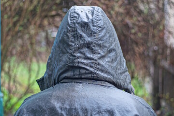 one man stands in a gray green wet jacket with a hood on his head in the rain on an autumn street