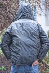 Fototapeta premium one man stands in a gray green wet jacket with a hood on his head in the rain on an autumn street