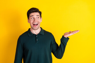 Young man in green polo smiling and gesturing enthusiastically against a vibrant yellow background