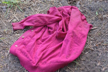garbage from one old red  dirty woolen sweater lies on the gray ground in the street