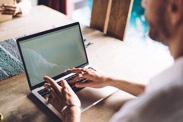 Cropped image of mal and female colleagues sitting at table together using modern technology for remote job, male freelancer typing on laptop computer with mock up screen share blog publications