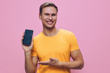 Smiling young caucasian man holding smartphone in yellow t-shirt on pink background digital nomad...