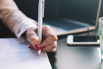Cropped image of female's hand writing with pen filling in application form for customer service survey in cafe, woman signing documentation and putting data on list with questions and answers