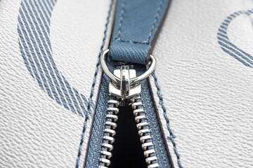 Close-up of an unzipped zipper on a white leather bag.