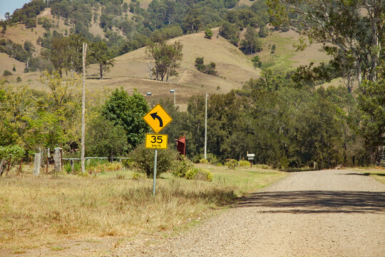 Road sign showing sharp bend ahead recommended speed 35 km per hour on gravel country road