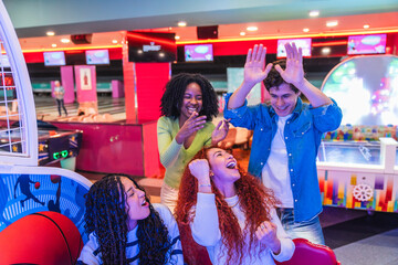 Cheerful multi ethnic friends enjoying arcade games and celebrating victory in a vibrant bowling alley
