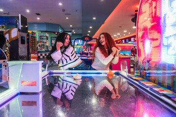 Two happy friends are enjoying their time playing air hockey in a vibrant arcade videogame room, celebrating their friendship and the thrill of the game