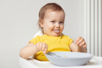 Baby girl  tasting new food, funny baby shows tongue at table, feed the little eater