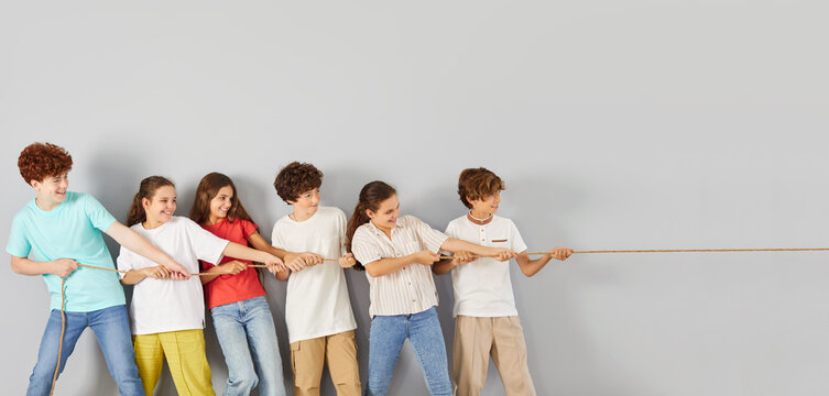 Diverse happy teen group team of cheerful classmates holding rope, playing tug of war, compete on common project enjoy laughing, kid team building activity, having fun enjoying activity playing to win
