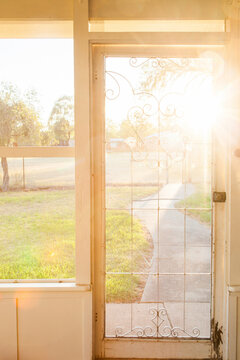 Flyscreen door on veranda of country homestead with morning sun light flare