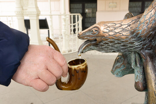 A hand holding a mug, pouring water from a healing spring in Karlovy Vary.