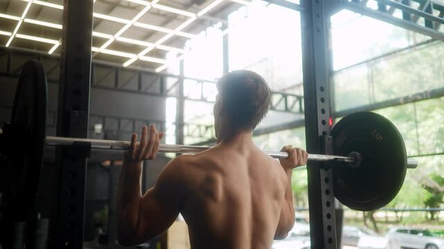 Athletic male fitness enthusiast with defined muscular back performing overhead barbell press exercise