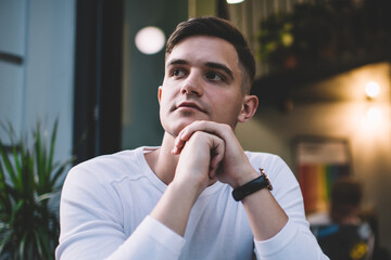 Thoughtful modern guy sitting in sidewalk cafe