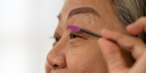 Beauty and Eyebrow Grooming. An elderly woman enhancing her eyebrows with a brush, showcasing her beauty routine.