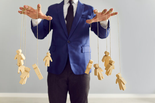 Boss and company leader pulls strings with little human shaped puppets as symbol of manipulating, influencing, exploiting, and violating rights of employees. Business, manipulation, control concept