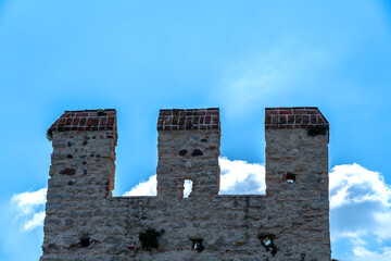 three battlements of an ancient Scaliger castle stand out against the light of an intensely blue...