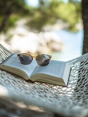Open book and sunglasses rest on a white hammock overlooking blurry beach nature background © scrdy