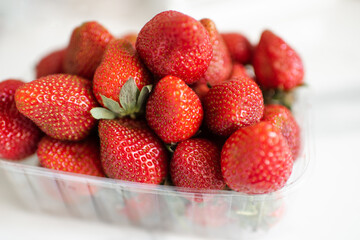 Plastic box full of ripe strawberries on kitchen table close up. Healthy eating.