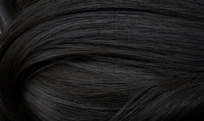 Brunette or black hair. Female long dark hair in black. Beautifully laid curls. Closeup texture in a dark key. Hairdressing, hair care and coloring. Shading gray hair. Background with copy space.