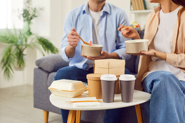 Young couple eating take-away food in boxes in the living room at home having lunch together....