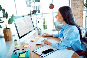 Young professional woman working in an office environment, viewing her screen attentively and staying focused, surrounded by modern decor