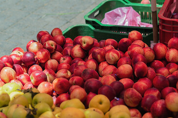 Red and yellow striped natural ripe fruit juicy delicious peaches and golden, green apples stacked on top of each other in a stall in the market on the background of fruit plastic boxes