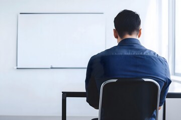 A pensive businessman in a blue shirt sits facing a blank whiteboard, symbolizing corporate challenges, new ideas, and strategic planning