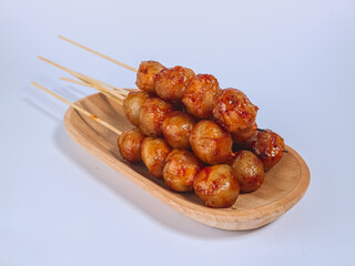 Spicy grilled meatballs on skewers served on a wooden plate, showcasing vibrant street food...