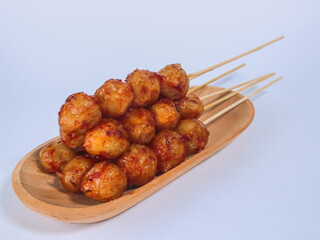 Spicy grilled meatballs on skewers served on a wooden plate, showcasing vibrant street food presentation on a clean white background