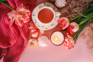 Flat lay of a cozy pink-themed setup with a gift box, flowers, candle, pink tea in a floral cup, white teapot, strawberries, and assorted sweets on a pink and fluffy background