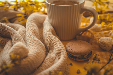 Close-up of a cozy scene with a textured beige blanket, a cup of coffee, a chocolate macaron,...