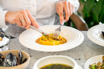 A close-up of a person dining in a restaurant, enjoying ravioli, mussels, and soup. The elegant table setting highlights the gourmet experience and culinary presentation.