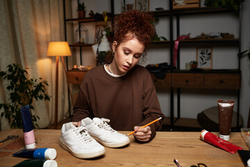 Creative young craftswoman transforming old sneakers into trendy personalized art at home