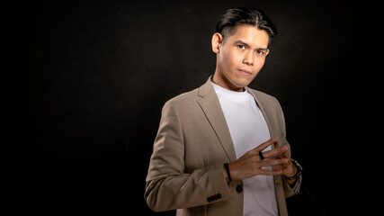 Asian man in beige blazer and white t-shirt forming steeple hands gesture with confident expression in studio with dark background, suitable for leadership, mastermind, or strategic branding themes