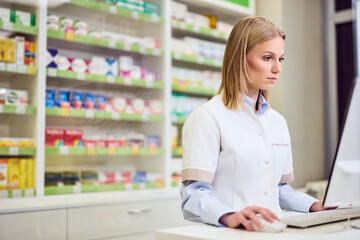 Pharmacist Working at Computer in Pharmacy Surrounded by Medicine Shelves